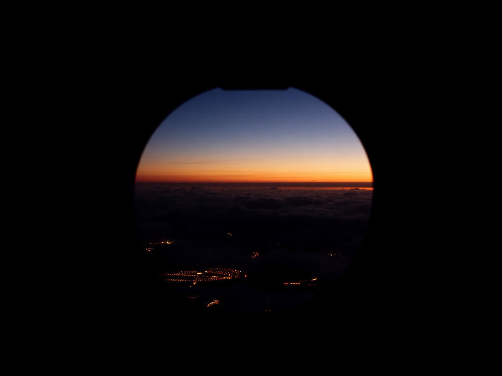 Vista pela janela oval de um jato privado ao entardecer com luzes de cidade abaixo